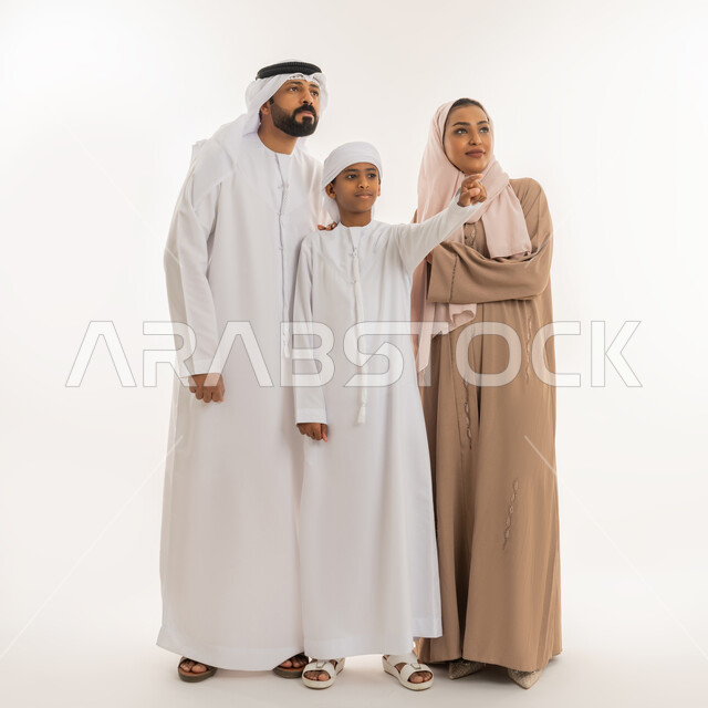 رعاية لآباء بالأبناء والاهتمام بهم، النظر الى مكان معين، التوجه والإشارة  لشيء ما، مفهوم لغة الجسد، بورتريه لولد عربي خليجي اماراتي رتدي الكندورة والعمامة يقف برفقة عائلته يشير بإصبع السبابة الى الأعلى دلالة على موقع محدد، صورة الجسم بالطول الكامل، خلفية بيضاء