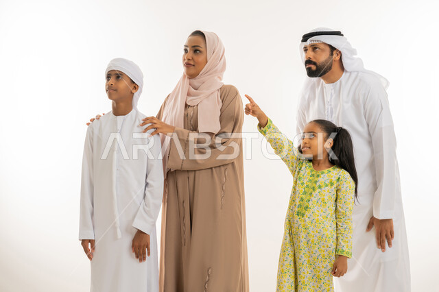 النظر الى مكان معين، التوجه والإشارة الى شيء ما، مفهوم لغة الجسد، بورتريه مقرب لفتاة عربية خليجية اماراتية ترتدي لباس الكاجوال تقف برفقة عائلتها  وتشير بإصبع السبابة الى الأعلى دلالة على موقع محدد، خلفية بيضاء