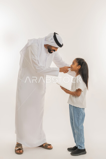 مشاهدة الأنشطة الترفيهية والتعليمية، دمج التعلم مع التقنية والتكنولوجيا، متابعة منصات التعليم الالكتروني المتاحة عبر الانترنت، بورتريه لفتاة عربية خليجية اماراتية ترتدي لباس الكاجوال تقف برفقة والدها وتستخدم الجهاز اللوحي، صورة الجسم بالطول الكامل، خلفية بيضاء