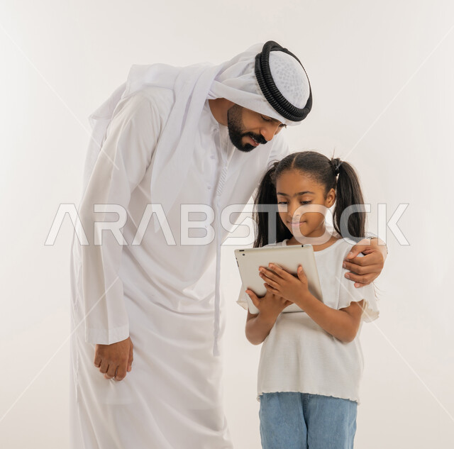 متابعة منصات التعليم الالكتروني المتاحة عبر الانترنت، دمج التعلم مع التقنية والتكنولوجيا، مشاهدة الأنشطة الترفيهية والتعليمية، بورتريه مقرب لفتاة عربية خليجية اماراتية ترتدي لباس الكاجوال تقف برفقة والدها وتستخدم الجهاز اللوحي، خلفية بيضاء