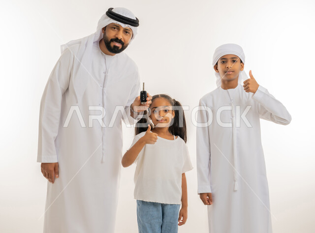 النظر للكاميرا بإيماءات السعادة، الحصول على رخصة القيادة، إقتناء سيارة جديدة، بورتريه مقرب لرجل عربي خليجي اماراتي يرتدي الكندورة والغترة يحمل بيده جهاز التحكم الالكتروني يقوم بمفاجأة ابنائه ويرفعون اصبع الابهام للأعلى بتعابير الاعجاب والرضا، خلفية بيضاء