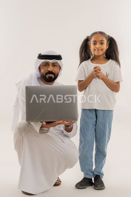 النظر للكاميرا بتعابير السعادة والسرور، التعلم عن بعد وتلقي الدروس عبر الأونلاين، استخدام التكنولوجيا والتقنية الحديثة والمتطورة، أنشطة ترفيهية الكترونية مسلية، بورتريه لرجل عربي خليجي اماراتي يرتدي الكندورة والغترة يقف برفقة ابنته ويستخدم الحاسوب، خلفية بيضاء