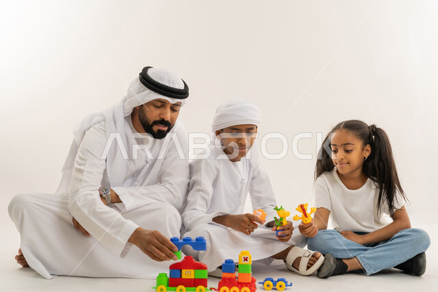 مشاركة اللحظات السعيدة والتسلية مع الأبناء، قضاء أوقات ممتعة مع الأولاد، الاستمتاع باللعب والأنشطة الترفيهية، بورتريه لأب عربي خليجي اماراتي يرتدي الكندورة والغترة يجلس على الأرض برفقة أبنائه بإيماءات السعادة والمرح، خلفية بيضاء