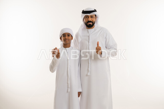 علامة الامتياز والجودة والنجاح، الشعور بالرضا والقبول، النظر الى الكاميرا بإيماءات السعادة والسرور، الاعجاب لتحقيق أمر معين، بورتريه مقرب لرجل عربي خليجي اماراتي يرتدي الكندورة والغترة يقف برفقة ابنه ويرفعوا اصبع الابهام الى الأعلى بتعابير الموافقة، خلفية بيضاء