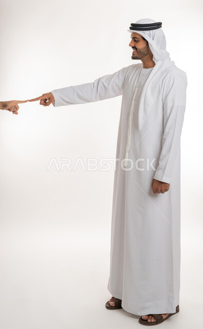 بناء علاقات و تكوين صداقات جديدة، الترحيب و السلام و إلقاء التحية، بورتريه لرجل عربي خليجي اماراتي يرتدي الكندورة والغترة البيضاء يقوم توجيه قبضة يده مقابل يد شخص آخر، ايماءات وحركات يدين تدل على التشجيع، صورة الجسم بالطول الكامل، خلفية بيضاء