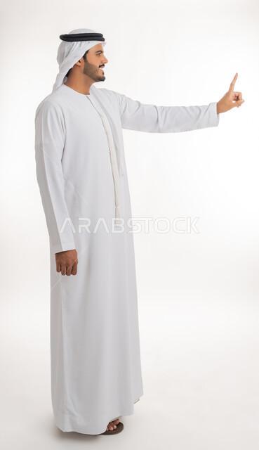 Indicating the location of an item, pointing and explaining something, specifying a specific location, portrait of an Arab Gulf Emirati man wearing a white kandura and ghutra pointing with his index finger to something, full body, white background