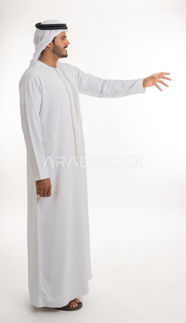 الإشارة إلى عنصر ما، بورتريه لرجل عربي خليجي اماراتي يرتدي الكندورة و الغترة البيضاء يمد يده للأمام يحاول التقاط عناصر هولوجرامية ثلاثية الأبعاد، محاولة الإحاطة والإمساك بشيء ما، الجسم بالطول الكامل، خلفية بيضاء