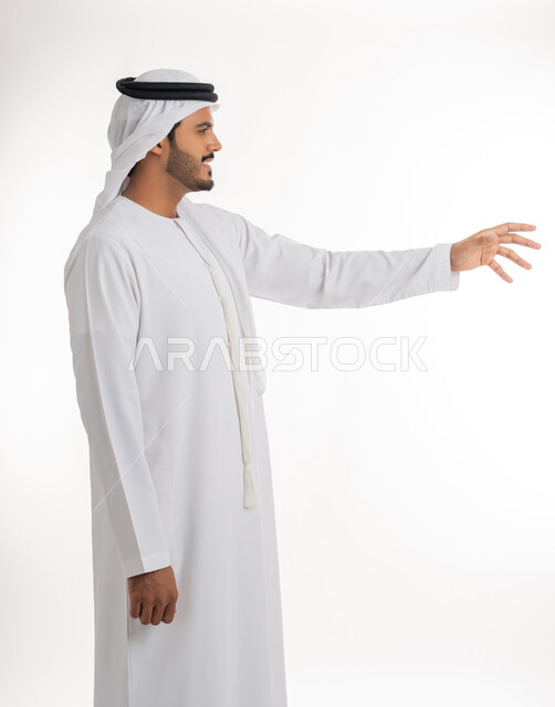 الإشارة إلى عنصر ما، بورتريه لرجل عربي خليجي اماراتي يرتدي الكندورة و الغترة البيضاء يمد يده للأمام يحاول التقاط عناصر هولوجرامية ثلاثية الأبعاد، محاولة الإحاطة والإمساك بشيء ما، الجسم بالطول الكامل، خلفية بيضاء