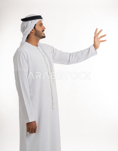 الإشارة إلى عنصر ما، بورتريه لرجل عربي خليجي اماراتي يرتدي الكندورة و الغترة البيضاء يمد يده للأمام يحاول التقاط عناصر هولوجرامية ثلاثية الأبعاد، محاولة الإحاطة والإمساك بشيء ما، الجسم بالطول الكامل، خلفية بيضاء