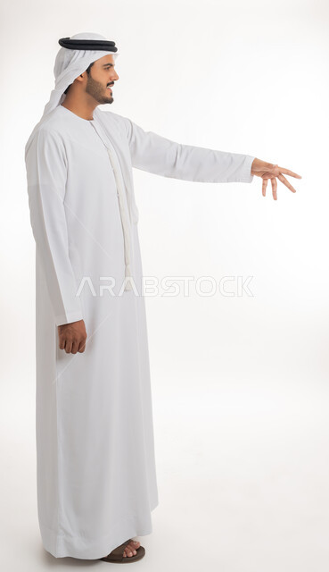 الإشارة إلى عنصر ما، بورتريه لرجل عربي خليجي اماراتي يرتدي الكندورة و الغترة البيضاء يمد يده للأمام يحاول التقاط عناصر هولوجرامية ثلاثية الأبعاد، محاولة الإحاطة والإمساك بشيء ما، الجسم بالطول الكامل، خلفية بيضاء