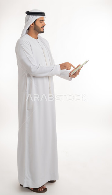 استعمال الجهاز اللوحي في إنجاز العمل، عرض شاشة كروما خضراء فارغة على الأجهزة التقنية، استعمال التكنولوجيا الحديثة والمتطورة للتعلم، بورتريه لرجل عربي خليجي اماراتي يرتدي الكندورة والغترة يمسك بيده تابلت، الجسم بالطول الكامل، خلفية بيضاء