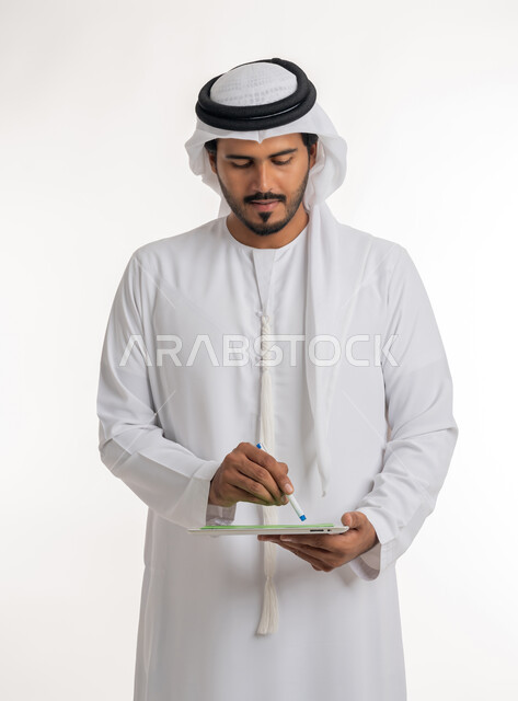 Using modern and advanced technology for learning, displaying a blank green chroma key screen on technical devices, using a tablet to complete work, close-up portrait of an Arab Gulf Emirati man wearing a kandura and ghutra holding a tablet in his hand, white background