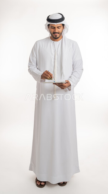 Using a tablet to complete work, displaying a blank green chroma key screen on technical devices, using modern and advanced technology for learning, portrait of an Arab Gulf Emirati man wearing a kandura and ghutra holding a tablet in his hand, full body, white background