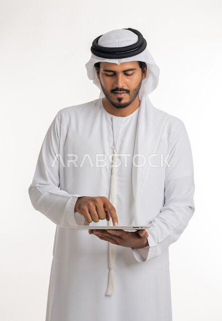 Using modern and advanced technology for learning, displaying a blank green chroma key screen on technical devices, using a tablet to complete work, close-up portrait of an Arab Gulf Emirati man wearing a kandura and ghutra holding a tablet in his hand, white background