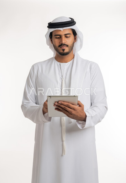 استعمال التكنولوجيا الحديثة والمتطورة للتعلم، عرض شاشة كروما خضراء فارغة على الأجهزة التقنية، استعمال الجهاز اللوحي في إنجاز العمل، بورتريه مقرب لرجل عربي خليجي اماراتي يرتدي الكندورة والغترة يمسك بيده تابلت، خلفية بيضاء