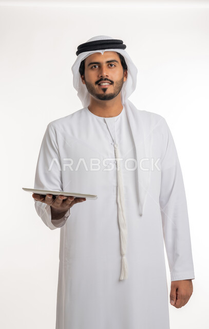 تطور التقنية والتكنولوجيا، عرض شاشة كروما خضراء فارغة على الأجهزة التقنية، استعمال الجهاز اللوحي في إنجاز العمل، بورتريه مقرب لرجل عربي خليجي اماراتي يرتدي الكندورة والغترة يمسك بيده تابلت، خلفية بيضاء