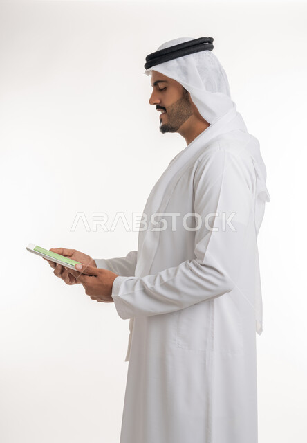 Technology and technology development, displaying a blank green chroma key screen on technical devices, using a tablet to complete work, close-up portrait of an Arab Gulf Emirati man wearing a kandura and ghutra holding a tablet in his hand, white background