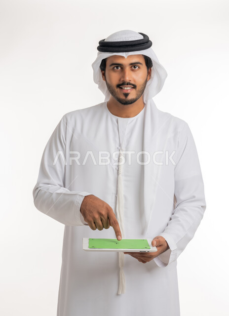 استعمال التكنولوجيا الحديثة والمتطورة للتعلم، عرض شاشة كروما خضراء فارغة على الأجهزة التقنية، استعمال الجهاز اللوحي في إنجاز العمل، بورتريه مقرب لرجل عربي خليجي اماراتي يرتدي الكندورة والغترة يمسك بيده تابلت، خلفية بيضاء