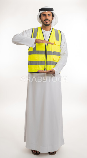 العمل في القطاع الهندسي، مفهوم الهندسة والانشاءات المعمارية، إحتواء وإمساك عنصر ما، بورتريه لمهندس عربي خليجي اماراتي يرتدي الكندورة والغترة البيضاء مع سترة الحماية يفتح يديه لعرض عناصرهولوجرامية ثلاثية الأبعاد، خلفية بيضاء