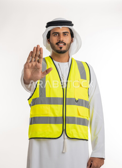 الرفض والامتناع والانزعاج, طلب التوقف وعدم الاقتراب, مفهوم الهندسة والانشاءات المعمارية، العمل في القطاع الهندسي، بورتريه لمهندس عربي خليجي امارتي يرتدي الكندورة والغترة البيضاء مع سترة الحماية يمد كفه نحو الأمام بإيماءات النهي, خلفية بيضاء