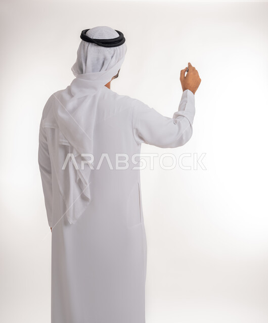 Using pens to mark objects and important points, preparing to write something on air, portrait of an Arab Gulf Emirati man wearing a white kandura using a pen to write down notes and ideas, white background