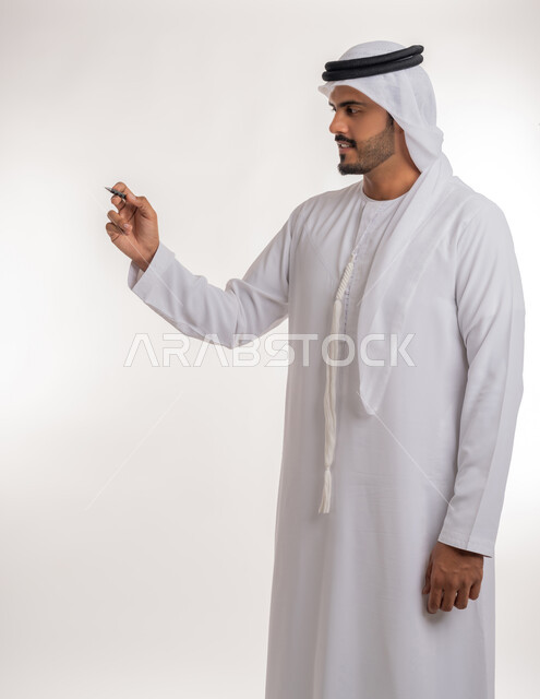 استخدام الأقلام  لتحديد الأشياء و النقاط المهمة، الإستعداد لكتابة شيء ما على الهواء، بورتريه لرجل عربي خليجي اماراتي يرتدي الكندورة البيضاء يستخدم القلم لتدوين الملاحظات والأفكار، خلفية بيضاء