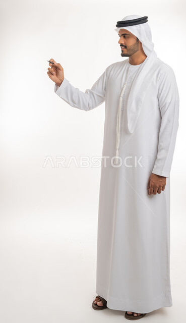 Using pens to mark objects and important points, preparing to write something on air, portrait of an Arab Gulf Emirati man wearing a white kandura using a pen to write down notes and ideas, white background