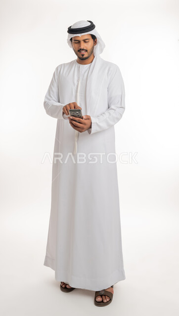 تصفح مواقع التواصل الاجتماعي عبر الانترنت، تطور التكنولوجيا والتقنيات الحديثة، بورتريه من الجانب لرجل اماراتي عربي خليجي يرتدي الكندورة والغترة يقوم باستخدام الهاتف المحمول، إجراء مكالمات فيديو عبر الجوال، صورة الجسم بالطول الكامل, خلفية بيضاء