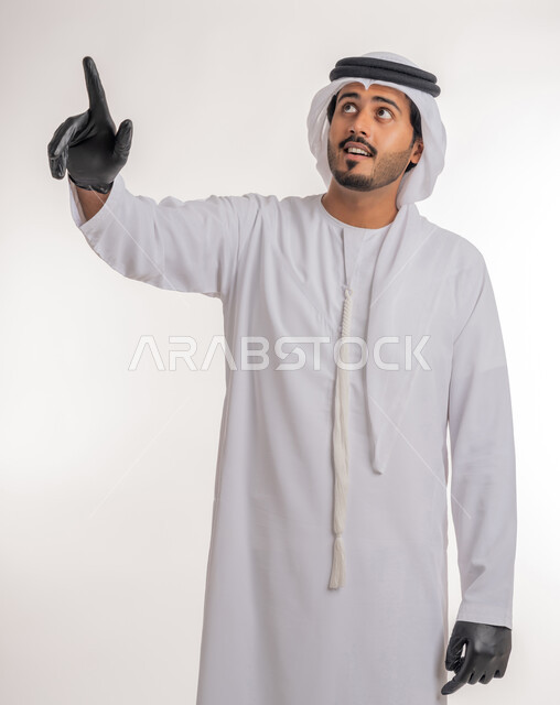 اشارات تحدد هذا المكان (هنا)، الاشارة إلى شيء ما، تعابير التحديد والتأكيد, بورتريه لرجل عربي خليجي اماراتي يرتدي الكندورة والغترة البيضاء مع قفازات الوقاية يقف باستقامة و يشير بأصابع السبابة للاختيار، خلفية بيضاء