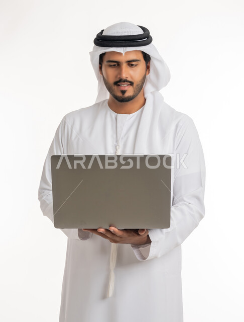 متابعة الأفلام والمسلسلات، تصفح مواقع التواصل الإجتماعي، الاجتهاد وانجاز الاعمال المطلوبة، بورتريه جانبي لرجل عربي خليجي اماراتي يرتدي الكندورة والغترة البيضاء يقف باستقامة يمسك بيده جهاز الحاسوب المحمول، استخدام التقنيات الحديثه والعمل عن بعد، خلفية بيضاء