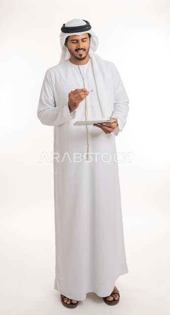Completing work tasks using a tablet device, Emirati companies and jobs, achieving company goals, the concept of integrating work with technology and technology, a side portrait of an Arab-Emirati Gulf man wearing a kandora with a ghutra, full-length body portrait, white background