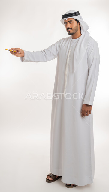 Using pens to mark objects and important points, preparing to write something on air, portrait of an Arab Gulf Emirati man wearing a white kandura using a pen to write down notes and ideas, white background