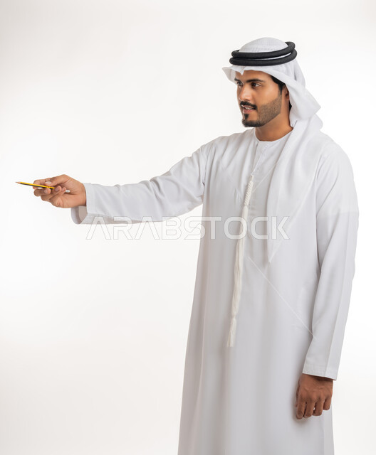 Using pens to mark objects and important points, preparing to write something on air, portrait of an Arab Gulf Emirati man wearing a white kandura using a pen to write down notes and ideas, white background
