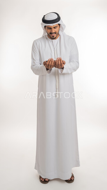 Increasing supplication in the holy month of Ramadan, striving in worship and maintaining obedience, portrait of an Arab Gulf Emirati man wearing a white kandura and ghutra, raising his hands and supplicating to God with gestures of supplication and entreaty, white background