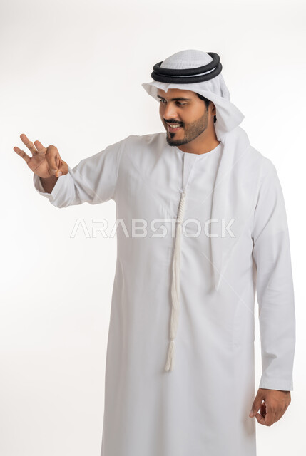 العرض والإمساك بشيء، الإشارة إلى عنصر ما، بورتريه لرجل عربي خليجي اماراتي يرتدي الكندورة و الغترة البيضاء يمد يده للأمام يحاول التقاط عناصر هولوجرامية ثلاثية الأبعاد، خلفية بيضاء