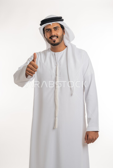 إيماءات وجه ويدين تدل على الموافقه والقبول، بورتريه مقرب لرجل عربي خليجي اماراتي يرتدي الثوب التقليدي الإماراتي والغترة البيضاء، يرفع أصبع الإبهام الى أعلى، الرضا بالنتيجه الإمتياز والتميز، الإعجاب والرضى والنجاح, خلفية بيضاء