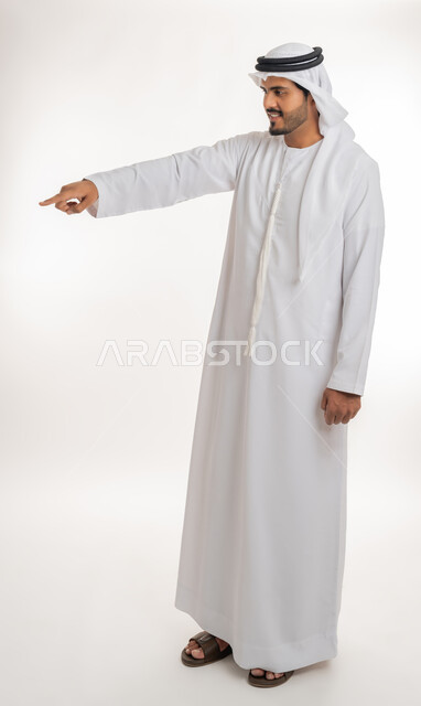 الإشارة و التوضيح إلى شيء ما, تحديد موقع معين, الدلالة على مكان عنصر، بورتريه لرجل عربي خليجي إماراتي يرتدي الكندورة و الغترة البيض يشير بإصبع السبابة إلى شيء ما، الجسم بالطول الكامل، خلفية بيضاء