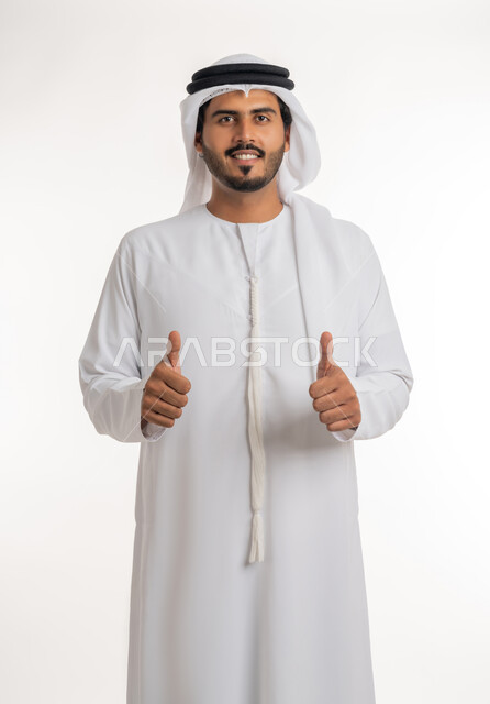إيماءات وجه ويدين تدل على الموافقه والقبول، بورتريه مقرب لرجل عربي خليجي اماراتي يرتدي الثوب التقليدي الإماراتي والغترة البيضاء، يرفع أصبع الإبهام الى أعلى، الرضا بالنتيجه الإمتياز والتميز، الإعجاب والرضى والنجاح, خلفية بيضاء
