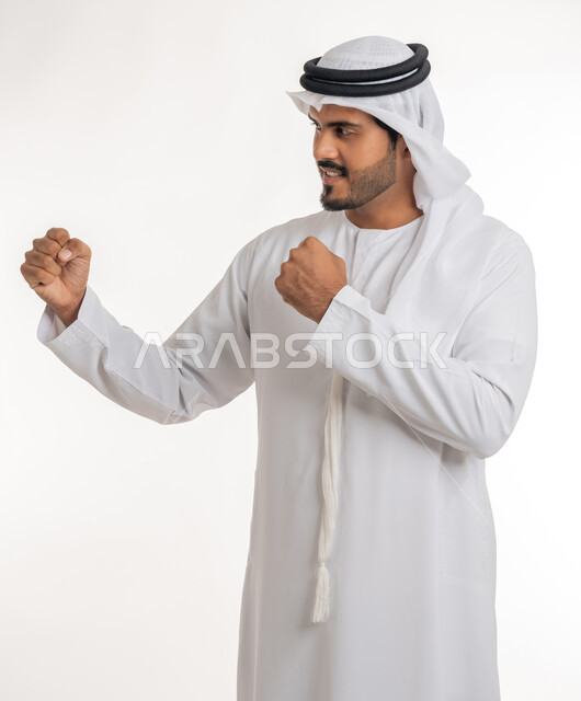 تعزيز صحة العظام والمفاصل، إتقان فنون الملاكمة، ممارسة رياضة الدفاع عن النفس، زيادة قدرة العضلات على التحمل، بورتريه من الجانب لرجل عربي خليجي اماراتي يرتدي الكندورة والغترة يرفع قبضات يديه بإيماءات القوة، خلفية بيضاء