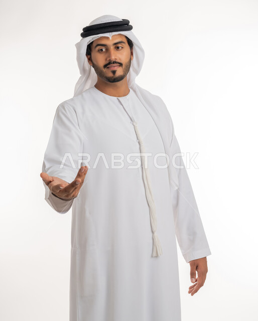 Showing and holding something, pointing to an item, portrait of an Arab Gulf Emirati man wearing a kandora and a white ghutra, extending his hand forward trying to capture three-dimensional holographic elements, white background