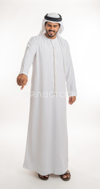 Pointing and explaining something, specifying a specific location, indicating the location of an item, portrait of an Arab Gulf Emirati man wearing a white kandura and ghutra pointing with his index finger to something, full body, white background