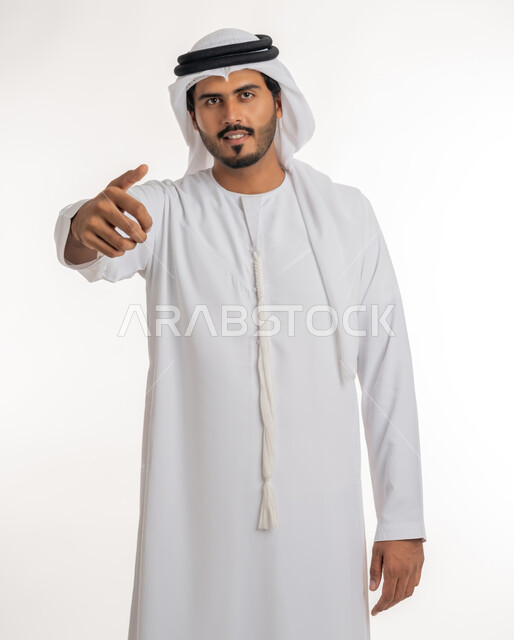 Indicating the location of an item, pointing and explaining something, specifying a specific location, portrait of an Arab Gulf Emirati man wearing a white kandura and ghutra pointing with his index finger to something, white background