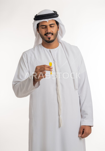 مفهوم التصويب والتركيز، الدقة في تحديد الهدف، هوايات ومهارات رياضية، التسلية والترفيه والتحدي في رمي السهام، بورتريه لرجل عربي خليجي اماراتي يرتدي الكندورة البيضاء يمسك سهم مغناطيسي أحمر اللون، خلفية بيضاء