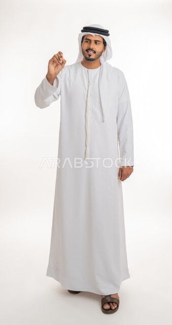 الإستعداد للكتابة وتحديد شيء ما, إيماءات يدين تدل على الإمساك بعنصر ما, بورتريه لمعلم عربي خليجي امارتي يرتدي الكندورة و الغترة يمسك بيده قلم, مفهوم التعليم بالمناهج المقررة، صورة الجسم بالطول الكامل, خلفية بيضاء