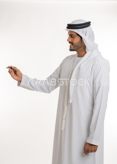 Hand gestures indicating holding an item, preparing to write and specifying something, close-up portrait of an Arab, Gulf, Emirati teacher wearing a kandora and ghutra, holding a pen in his hand, the concept of education according to the prescribed curricula, white background.
