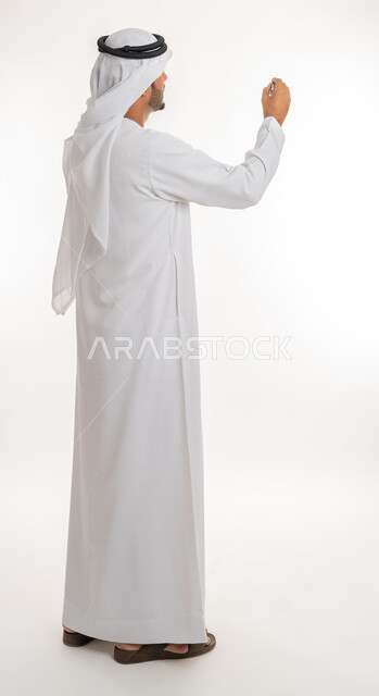 الإستعداد للكتابة وتحديد شيء ما, إيماءات يدين تدل على الإمساك بعنصر ما, بورتريه من الخلف لمعلم عربي خليجي امارتي يرتدي الكندورة و الغترة يمسك بيده قلم, مفهوم التعليم بالمناهج المقررة، صورة الجسم بالطول الكامل, خلفية بيضاء