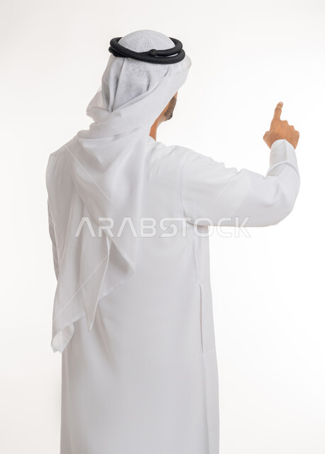الإشارة إلى عنصر ما، بورتريه مقرب من الخلف لرجل عربي خليجي اماراتي يرتدي الكندورة والغترة البيضاء يرفع يده للاعلى يشير بأصبع السبابة الى هدف محدد، خلفية بيضاء