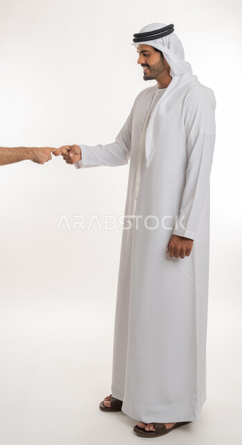 مفهوم الاستقبال والترحيب، إلقاء التحيه والسلام، بورتريه لرجل عربي خليجي إماراتي يرتدي الكندورة والغترة  يمد يده بإيماءات المصافحة، التعارف و الصداقه وتكوين العلاقات،  صورة الجسم بالطول الكامل, خلفية بيضاء