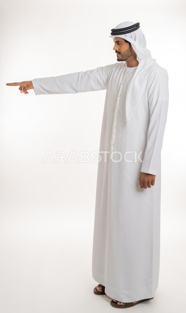 الإشارة و التوضيح إلى شيء ما, تحديد موقع معين, الدلالة على مكان عنصر، بورتريه لرجل عربي خليجي إماراتي يرتدي الكندورة و الغترة البيض يشير بإصبع السبابة إلى شيء ما، الجسم بالطول الكامل، خلفية بيضاء