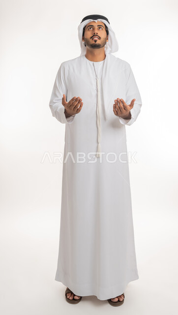 العبادة وترديد الأدعية بإيماءات الخضوع، الدعاء ورفع اليدين إلى السماء، بورتريه لرجل عربي خليجي إماراتي يرتدي الكندورة والغترة يرفع يديه وينظر للأعلى بتعابير التضرع لله تعالى، الجسم بالطول الكامل، خلفية بيضاء